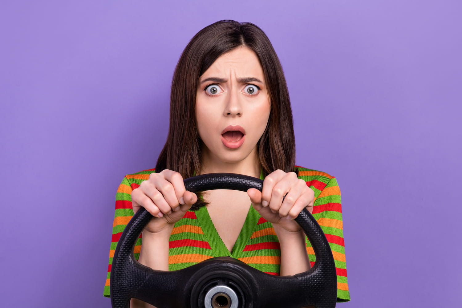 Portrait of astonished speechless girl holding steering wheel isolated on violet background.