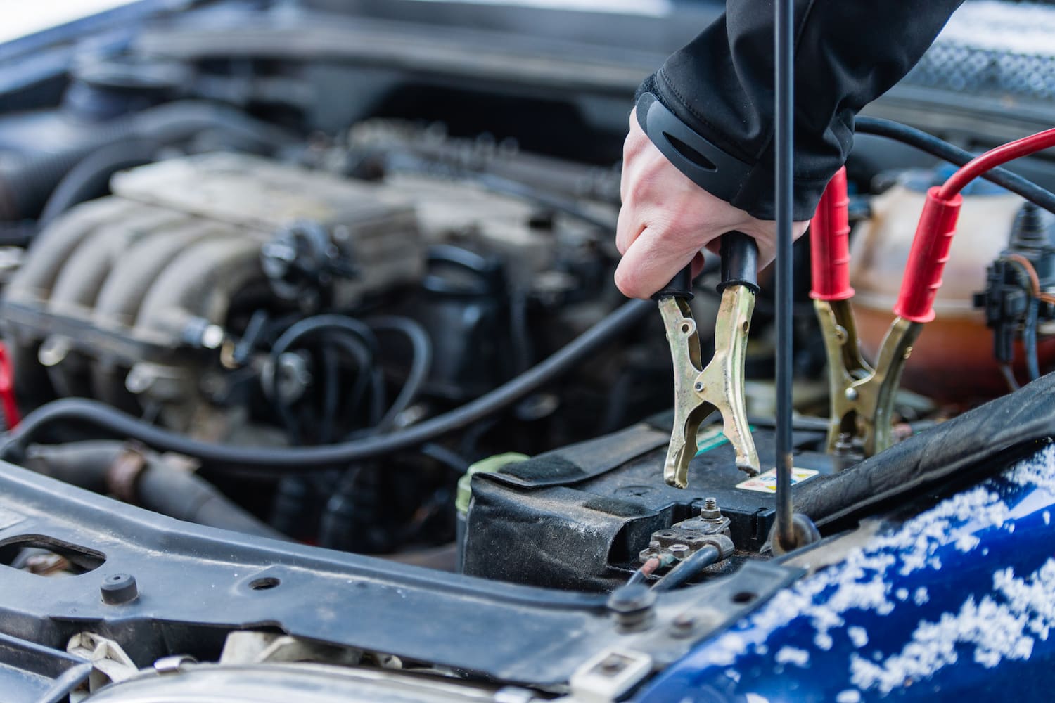 Person using booster cables to jump start a car battery.
