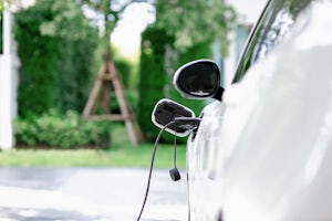 Closeup of white electric vehicle plugged-in with charging cable