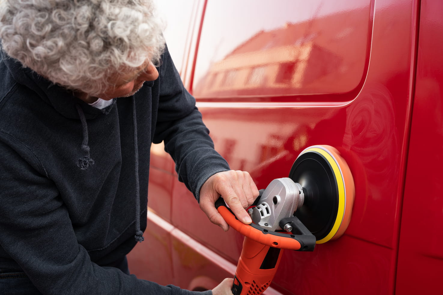 A mature person polishing a car with an electric orbital polisher