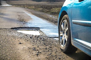 Blue car driving next to a winter pothole on open road