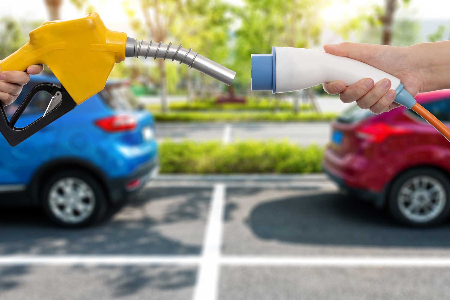 Human hands holding electric plug and gasoline nozzle against one another