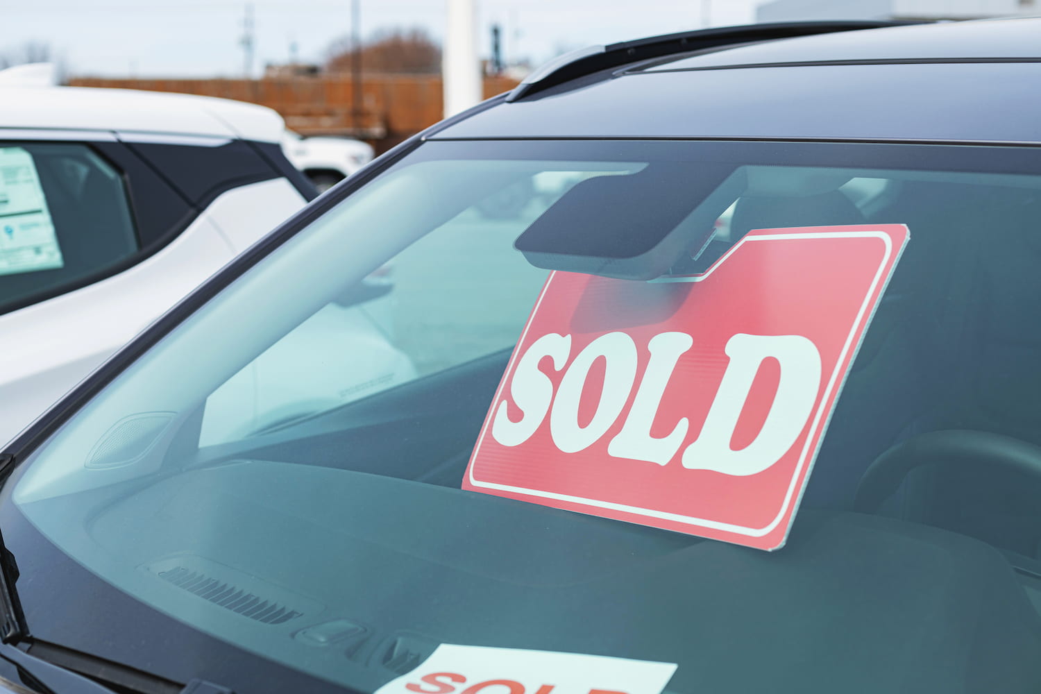 A "Sold" sign displayed on the windshield of a car in a dealership parking lot.