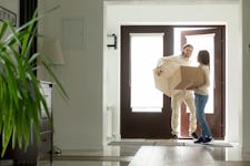 Happy young couple carrying cardboard boxes opening door entering inside modern own house.