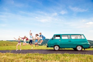Teenagers jumping next to a campervan against green nature and blue sky