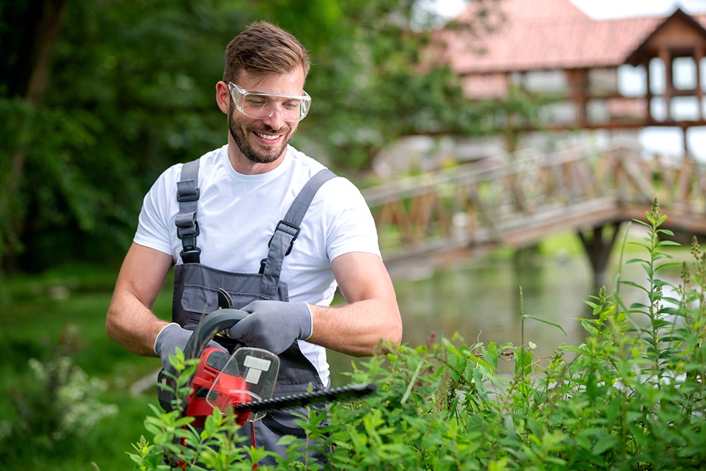 A person appears pleased while holding lawn care equipment and wearing safety goggles.