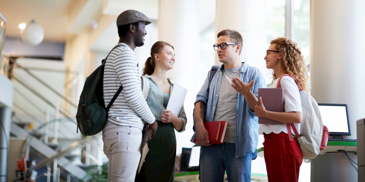 A group of young individuals standing in an academic setting, holding books and wearing backpacks.
