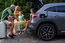 A family with little children loading their electric car with beach picnic luggage and waiting as the car is charging