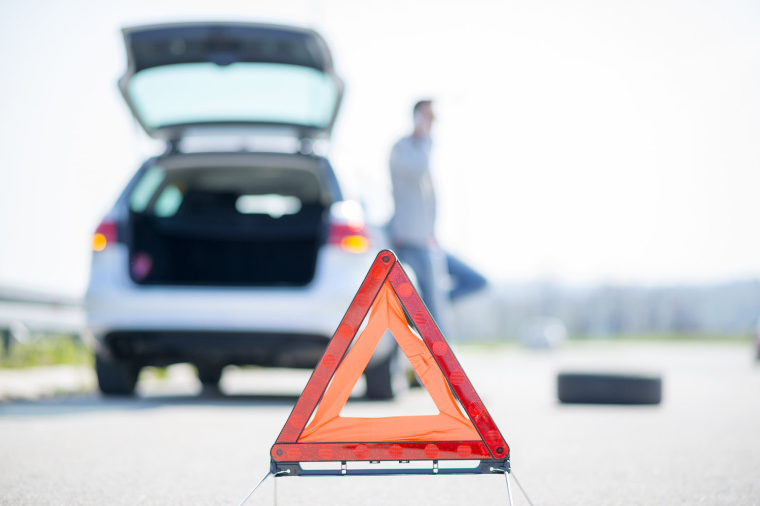 An individual sets up a warning triangle next to their parked silver car on the roadside.