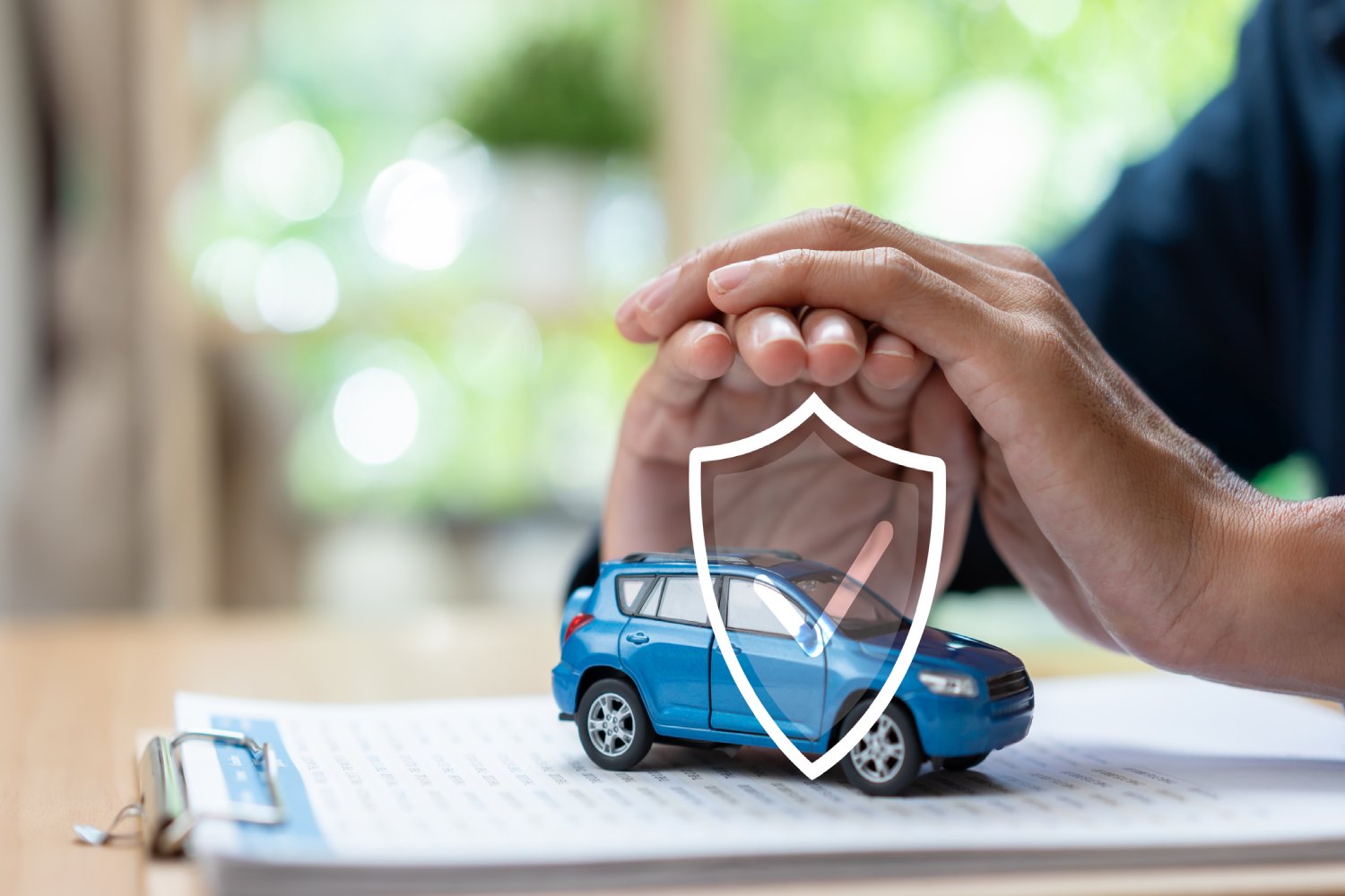 Person holding hands over miniature car with shield symbol over it.