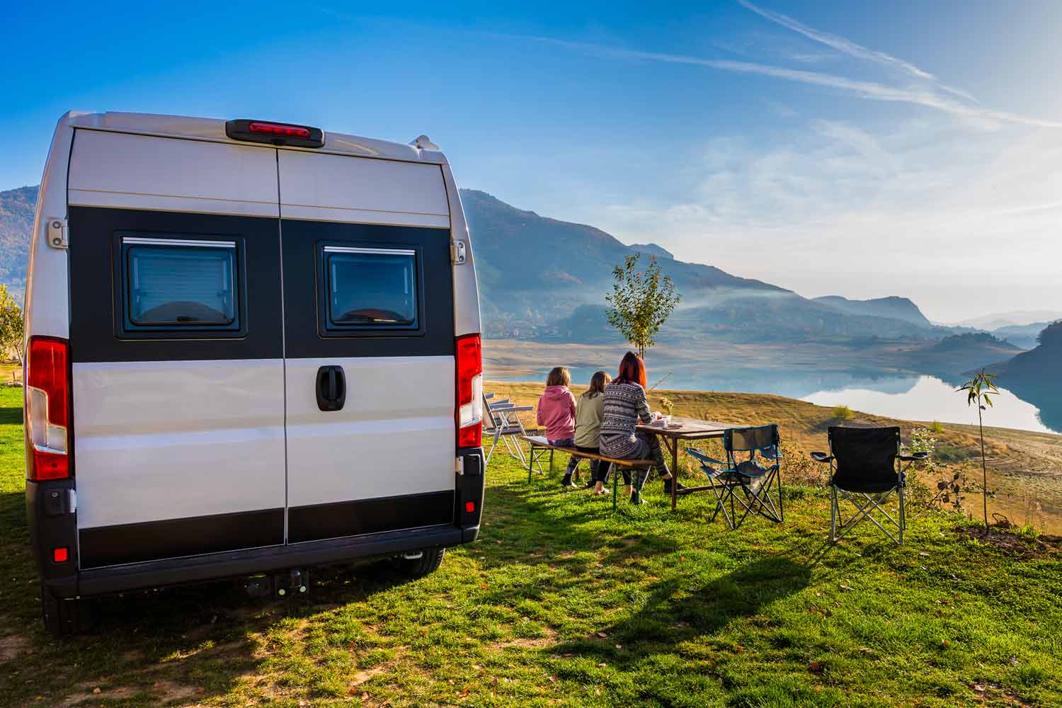 Family enjoying breakfast outside their camper van during a road trip.