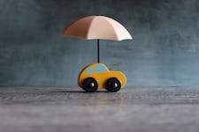 Umbrella and a yellow toy car on a table with teal background