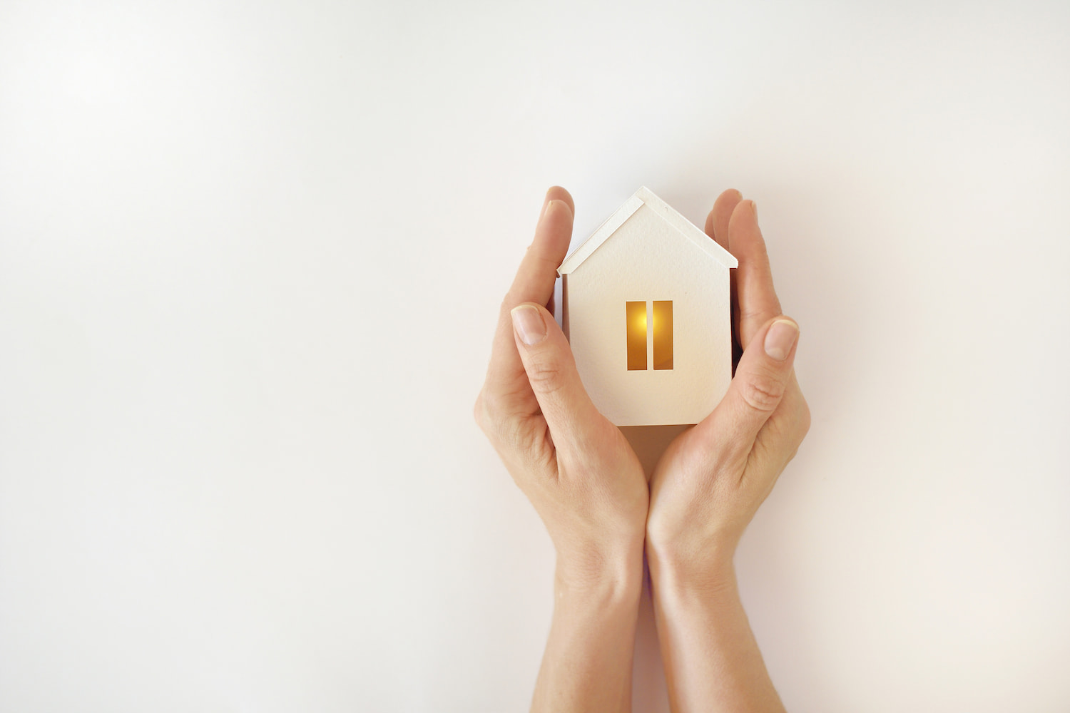 Hand holding a model house with warm lights inside on a white background.