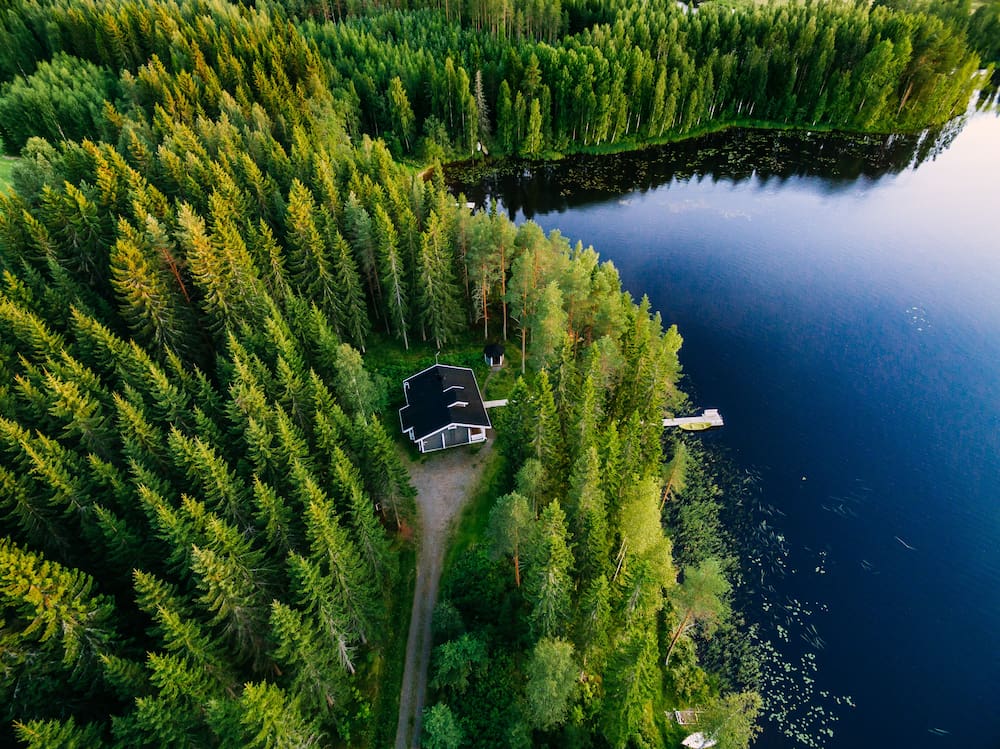 Aerial view of a cabin nestled in a forest with an ocean nearby.