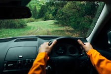 Driver dressed bright orange jacket driving a modern off road right hand drive RHD car on the mountain green forest country road.
