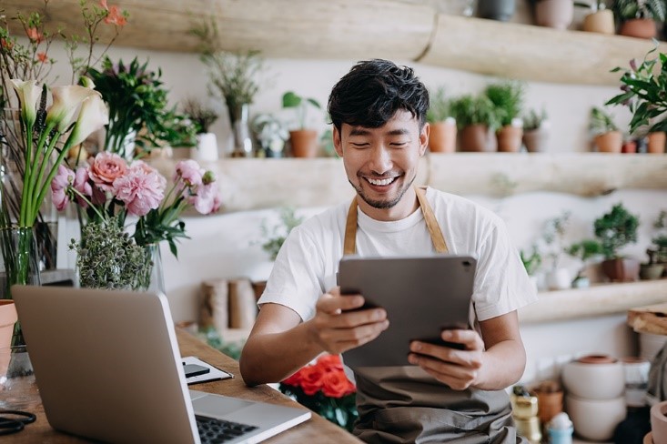 A cheerful individual in an apron standing in a plant and flower shop.