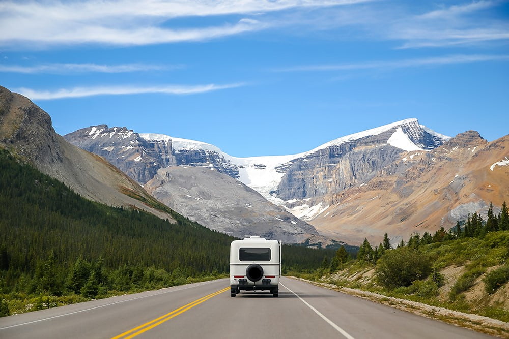 Driving a RV along a highway bordered by scenic mountains.