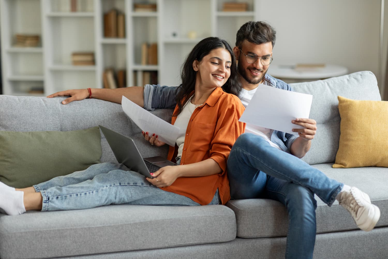 Happy couple reviewing documents while sitting on a couch, looking at an agreement or certificate.
