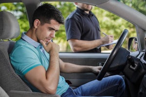 Young driver in car looking worried next to an officer who is writing a traffic ticket