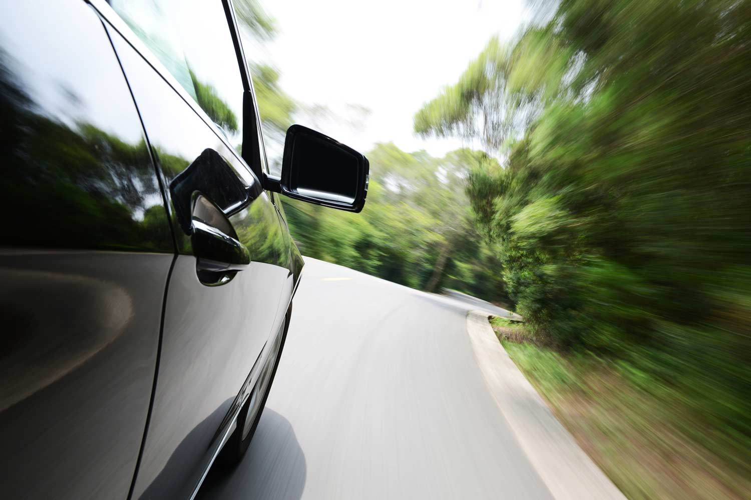 Black car driving fast on a narrow mountain road.