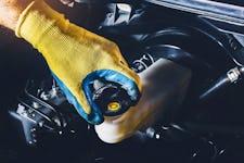 A mechanic's gloved hand opening the car's brake fluid reservoir cap to check the brake fluid level