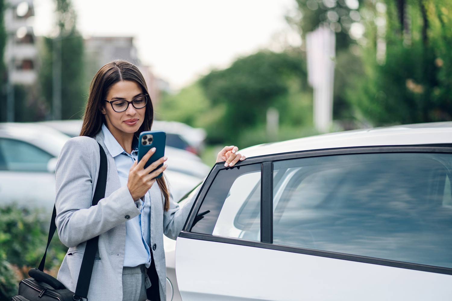 A woman in formal wear using her phone while getting out of her car
