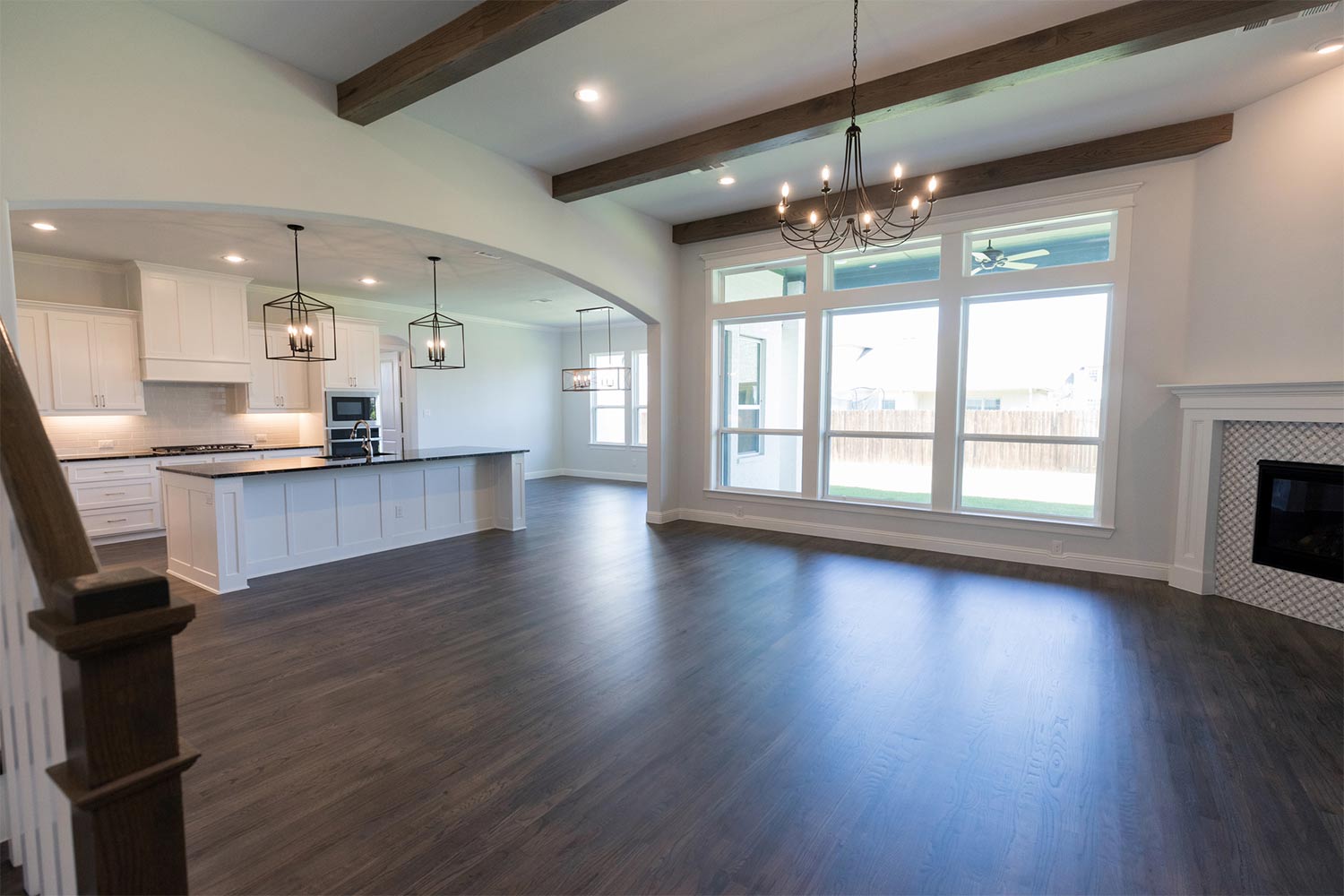 Empty living area and kitchen inside of a new modern home. The sun shines through lare windows in the living area.