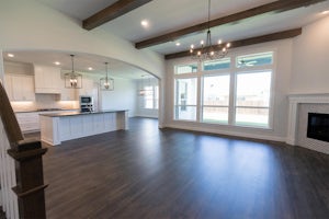 Empty living area and kitchen inside of a new modern home. The sun shines through lare windows in the living area.
