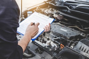Automobile mechanic repairman checking a car engine with while writing to a clipboard