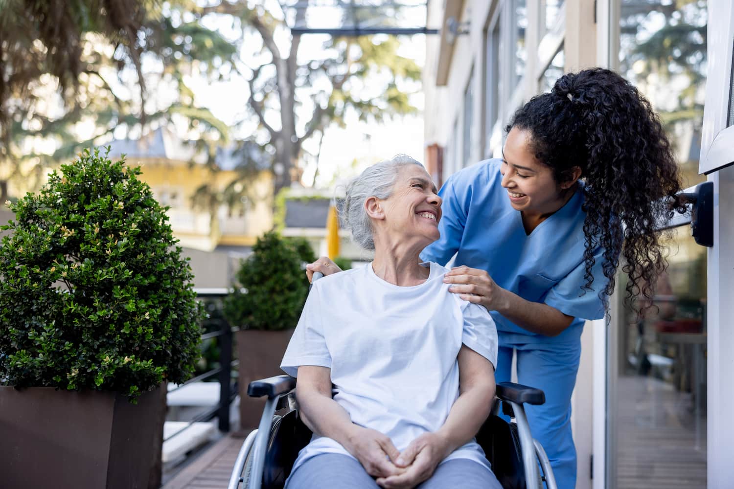 Caregiver helping a senior person in a wheelchair, both smiling.