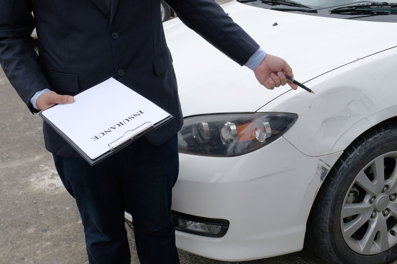 A person holding a pen is pointing at a visibly damaged car next to him.