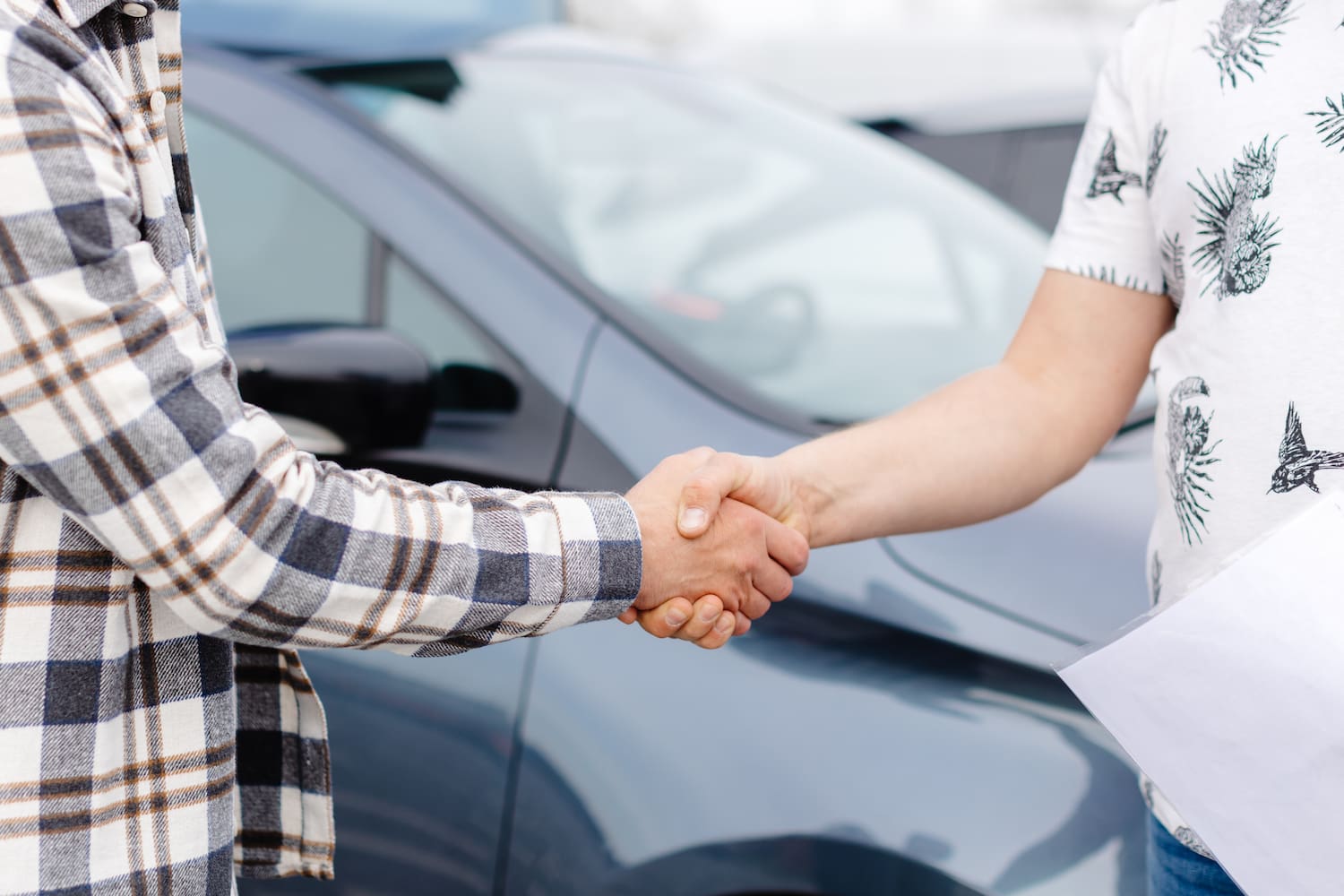 Two people shaking hands against a blurred car.