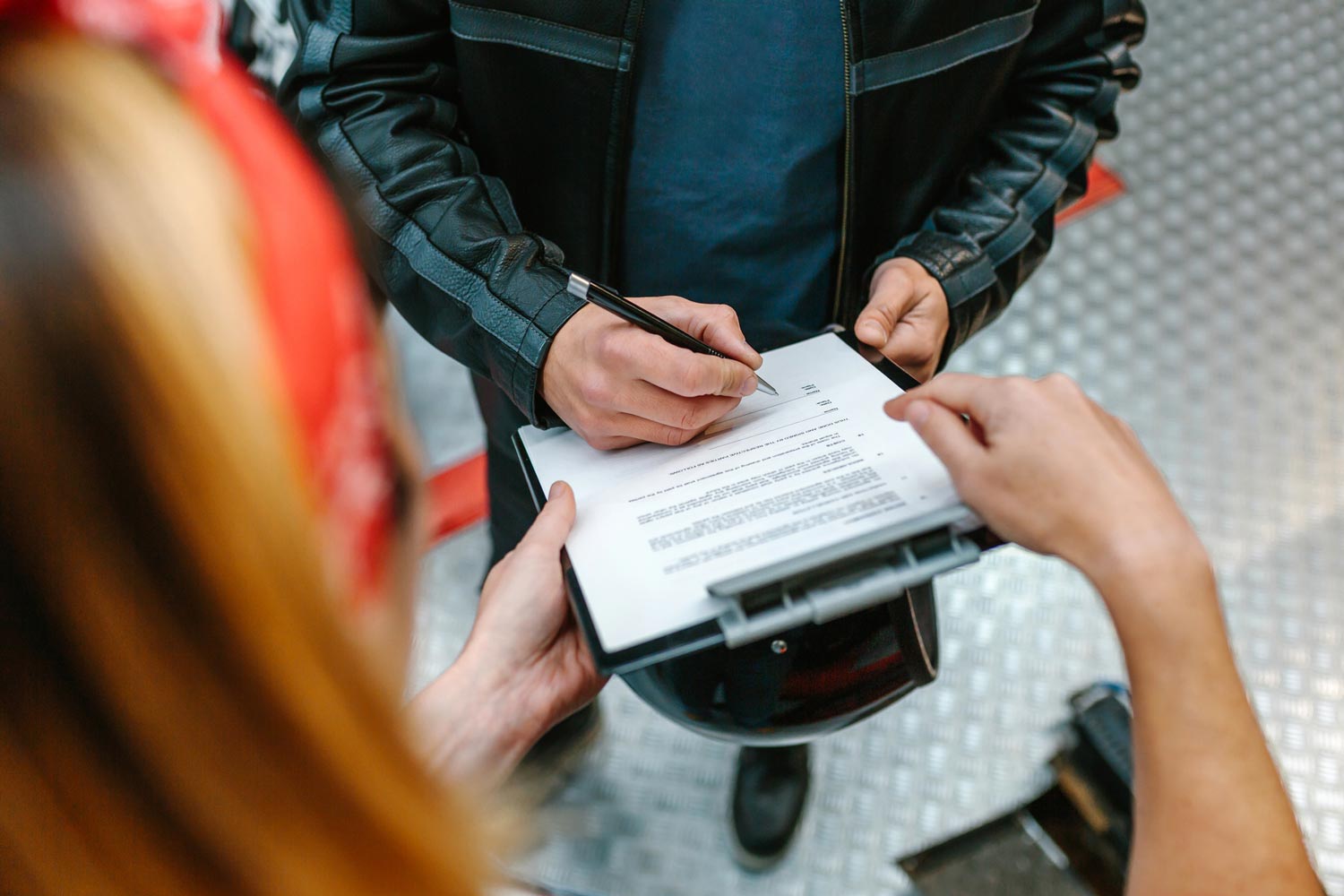 A mechanic holding a clipboard while a customer signs a form in a workshop.