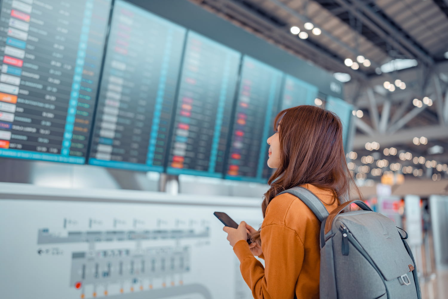 Women at the airport holding a cellphone and looking at flight times.