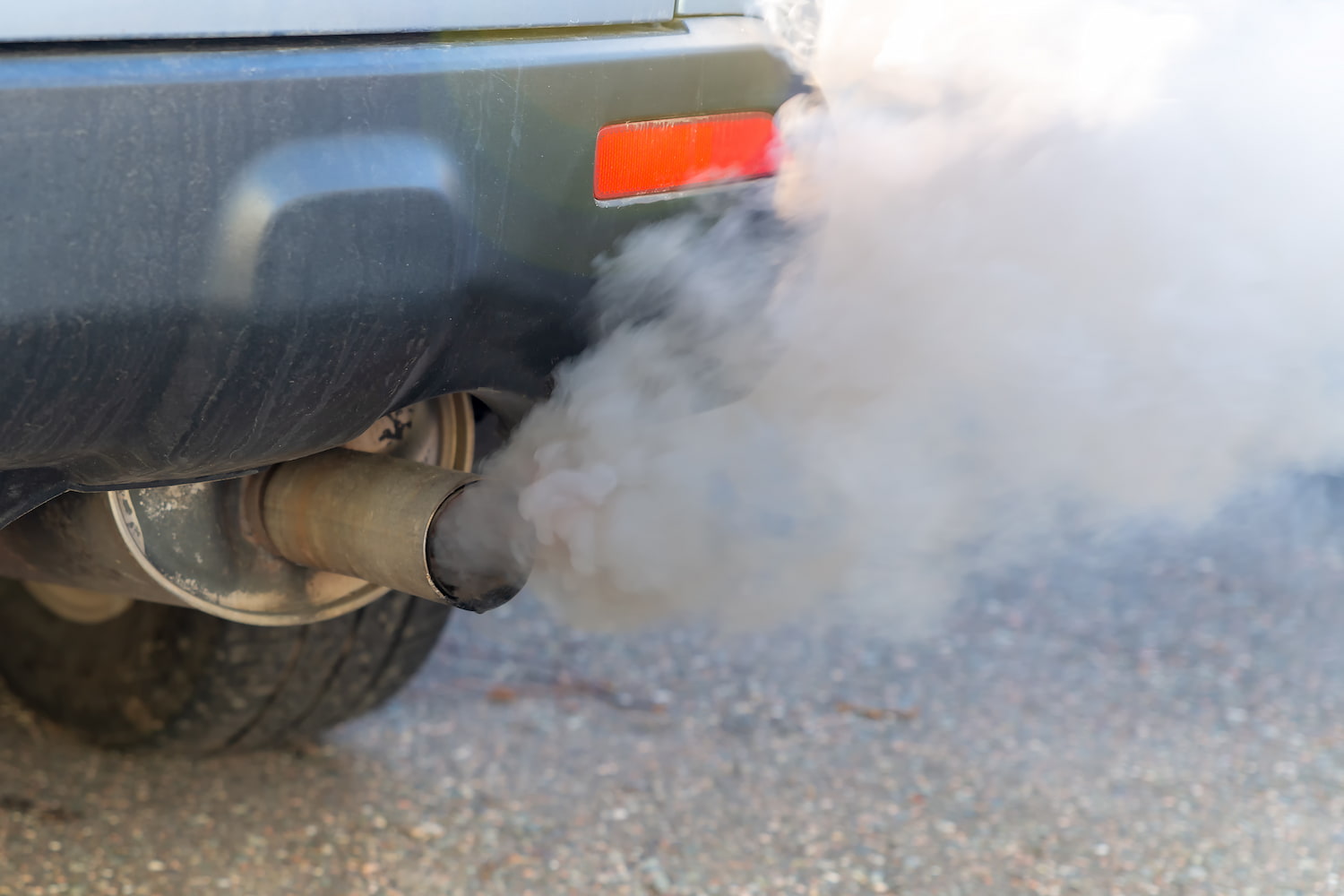 Thick smoke emits from a car's exhaust pipe. Close-up with shallow depth of field.