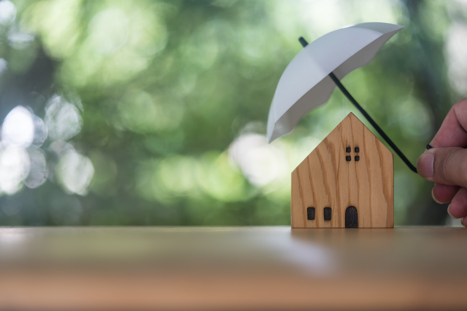 Small white umbrella over a wooden house model, home insurance concept.