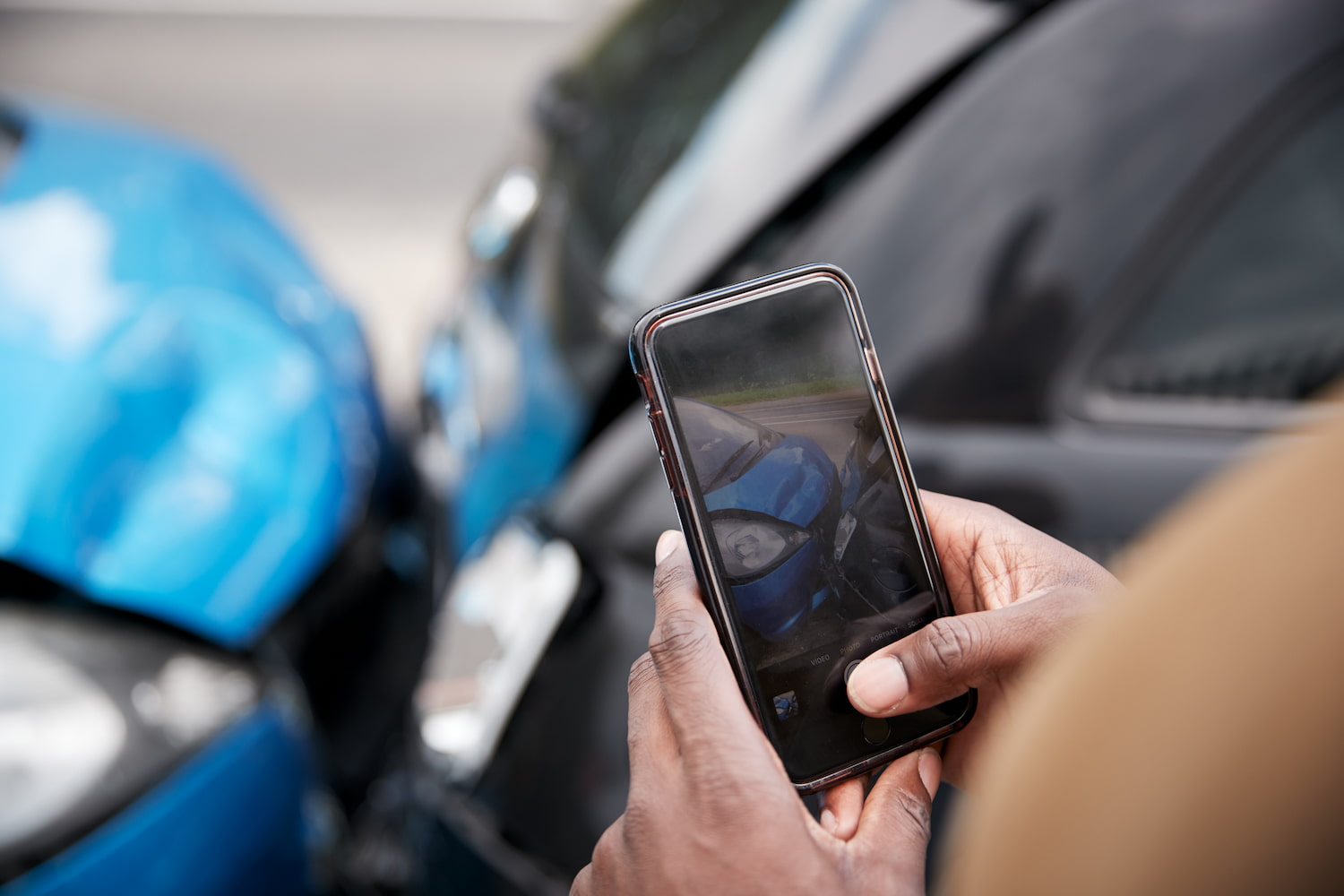 A closeup of a man's hands taking a photo with a phone of car collision