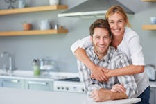 Portrait of a wife hugging her smiling husband from behind while relaxing together in their kitchen at home