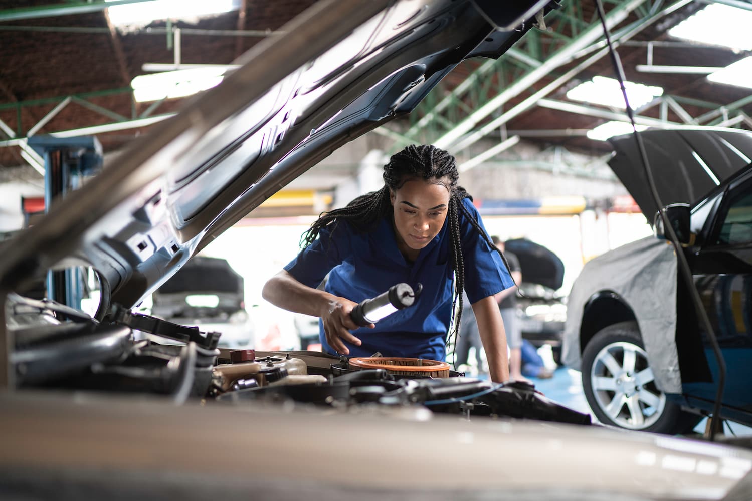 Woman repairing a car in auto repair shop.