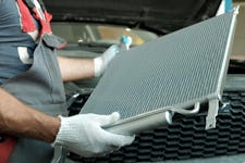 An auto mechanic holding a car radiator in a repair shop