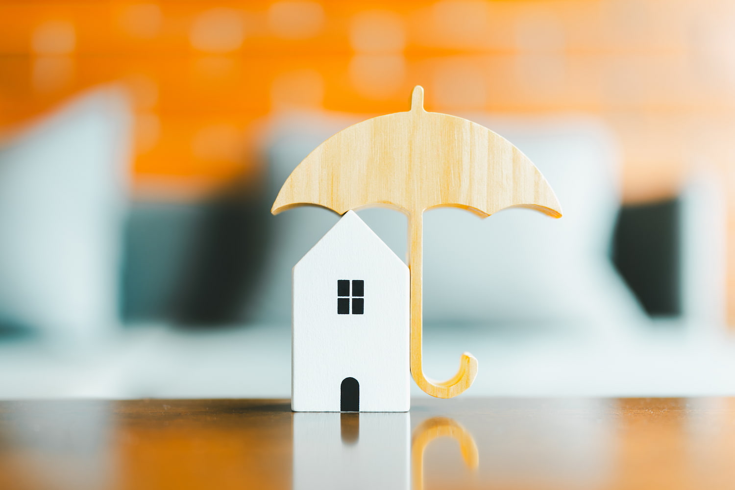 Umbrella over a miniature house on a table, indicating home insurance and risk protection.