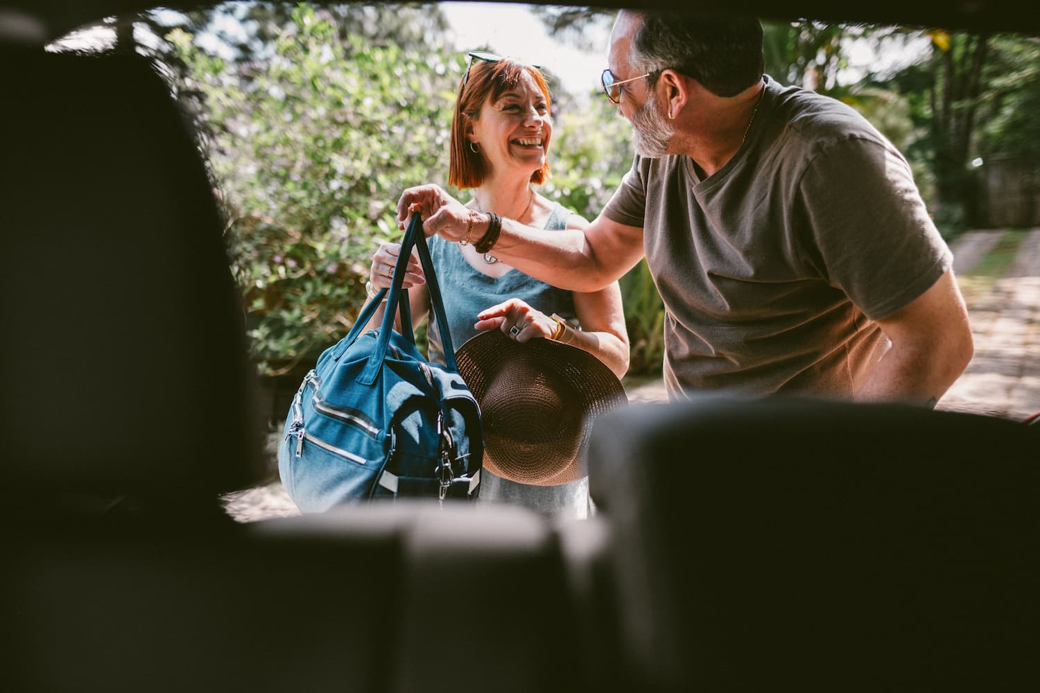 Smiling mature couple packing their luggage into the trunk of their car