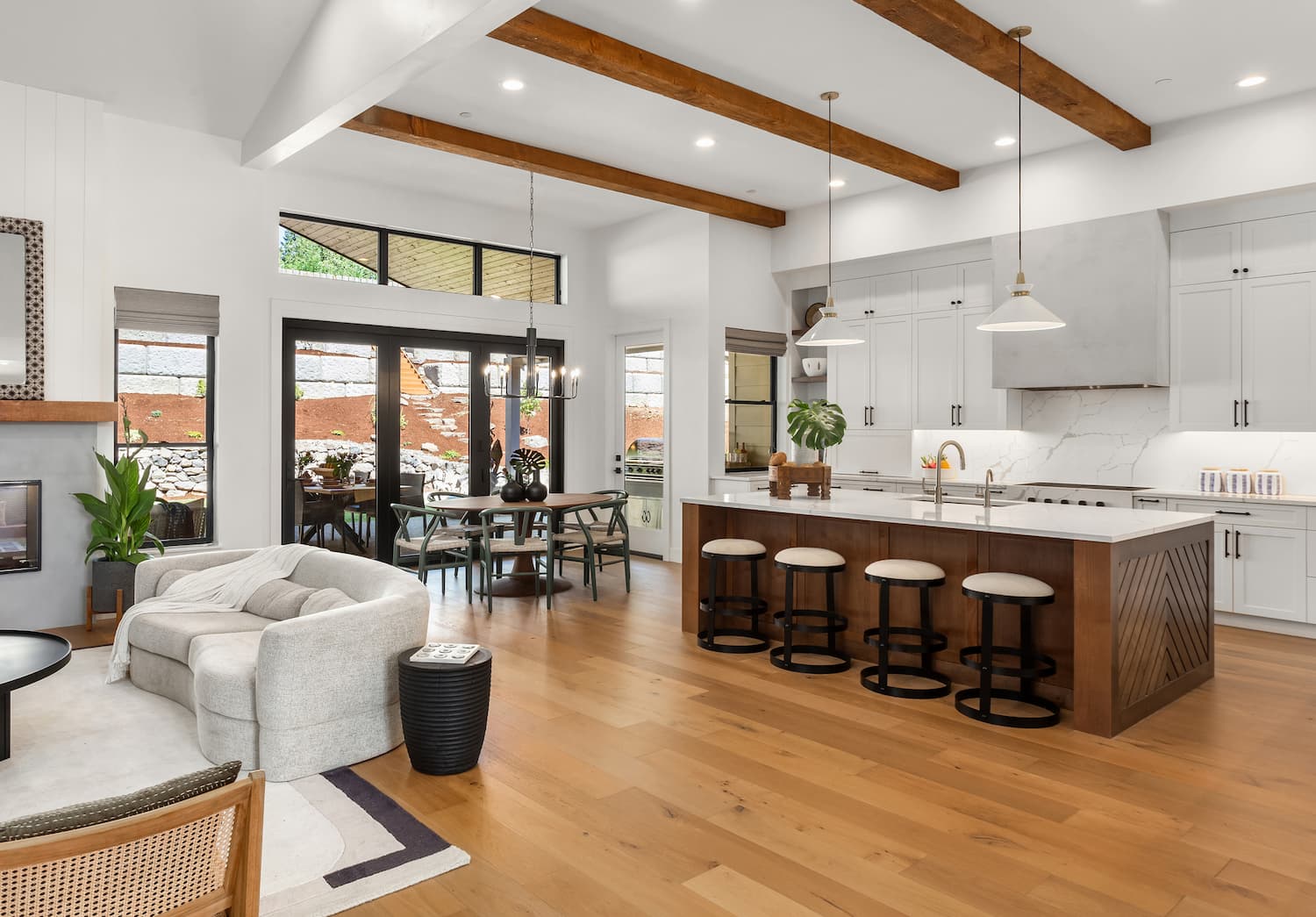 Beautiful living room and kitchen in new luxury home with white cabinets, wood beams, pendant lights and hardwood floors.