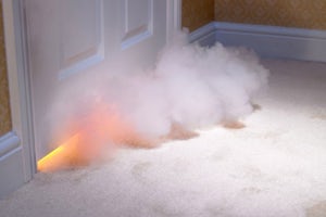 A close up of a smoke cloud below a closed door of a room on fire