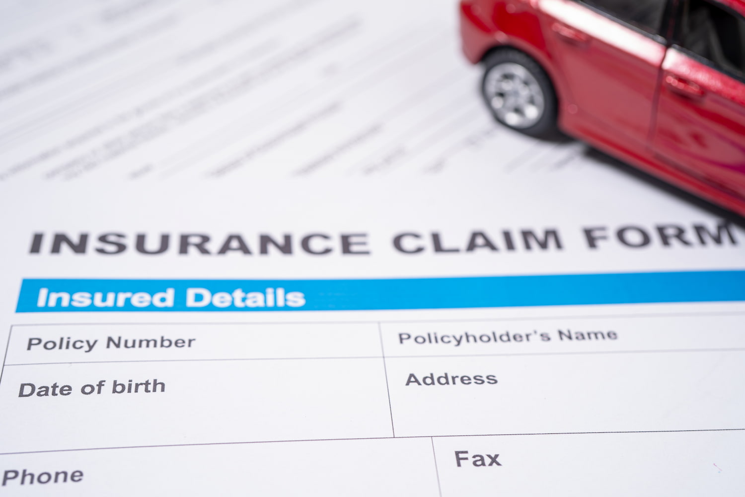 A red toy car positioned on top of an insurance claim form.