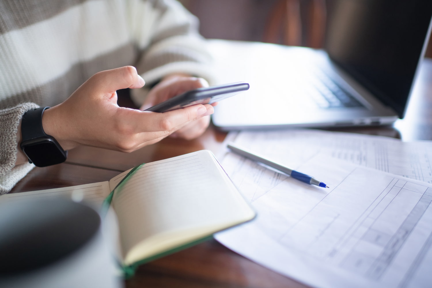 Person with smartphone and laptop reviewing documents.