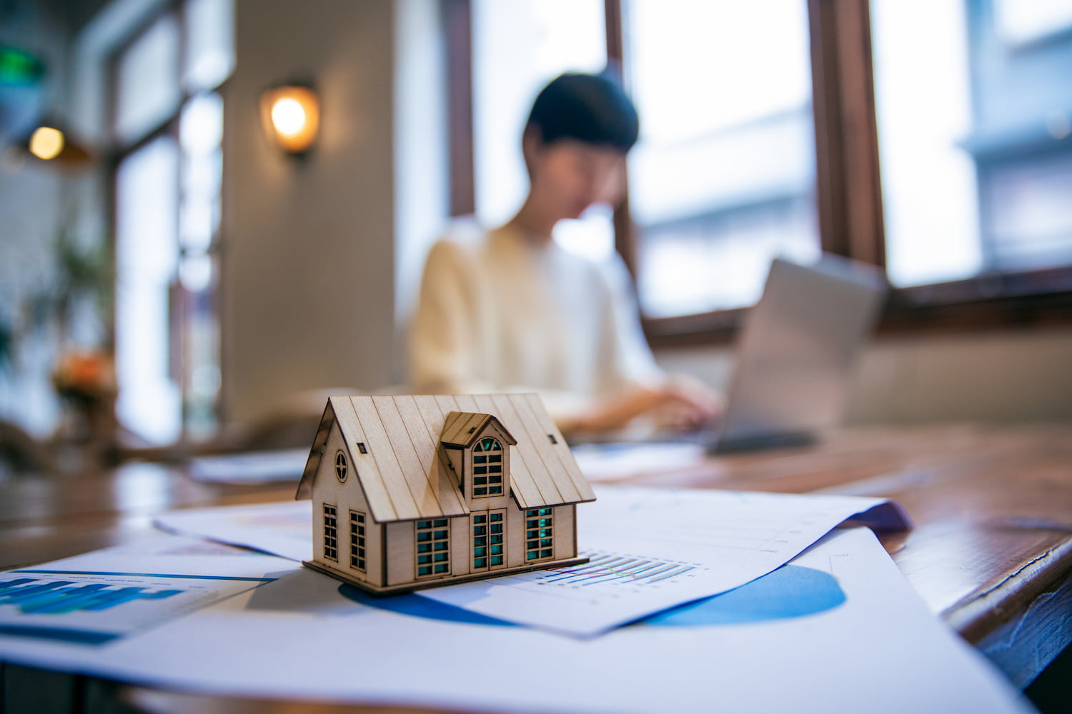 A person working on a laptop with a model house on the table.