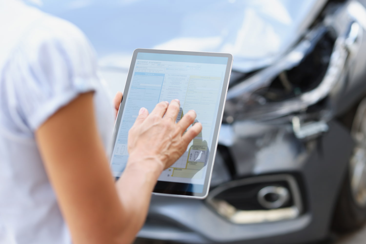 Person filling out form on digital tablet against background of broken car closeup.