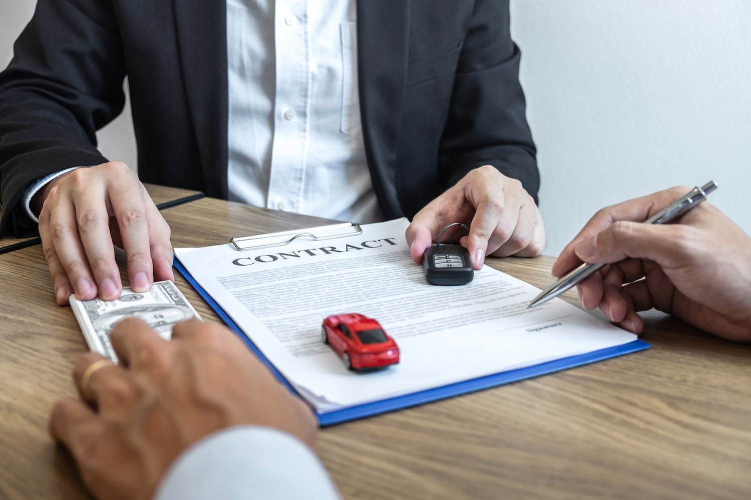 A person hands over car keys to another after receiving payment and signing the contract.