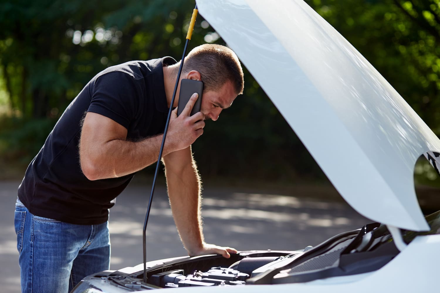 Man calling someone for help with his broken car. His white car's hood is open.